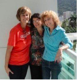 Três mulheres estão posando para uma foto juntas e uma delas está vestindo uma blusa laranja.