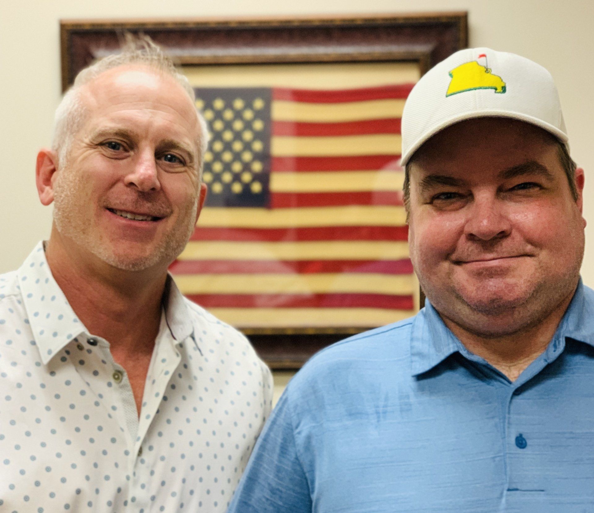 Two men are standing next to each other in front of an american flag.