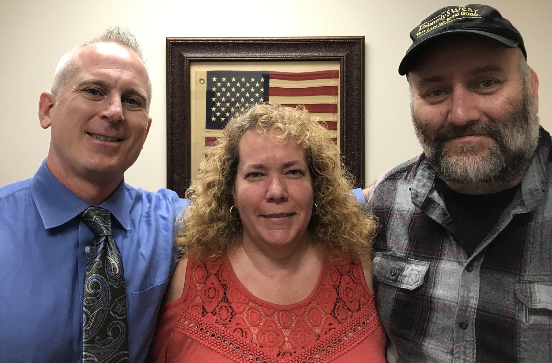 Two men and a woman are posing for a picture in front of an american flag.