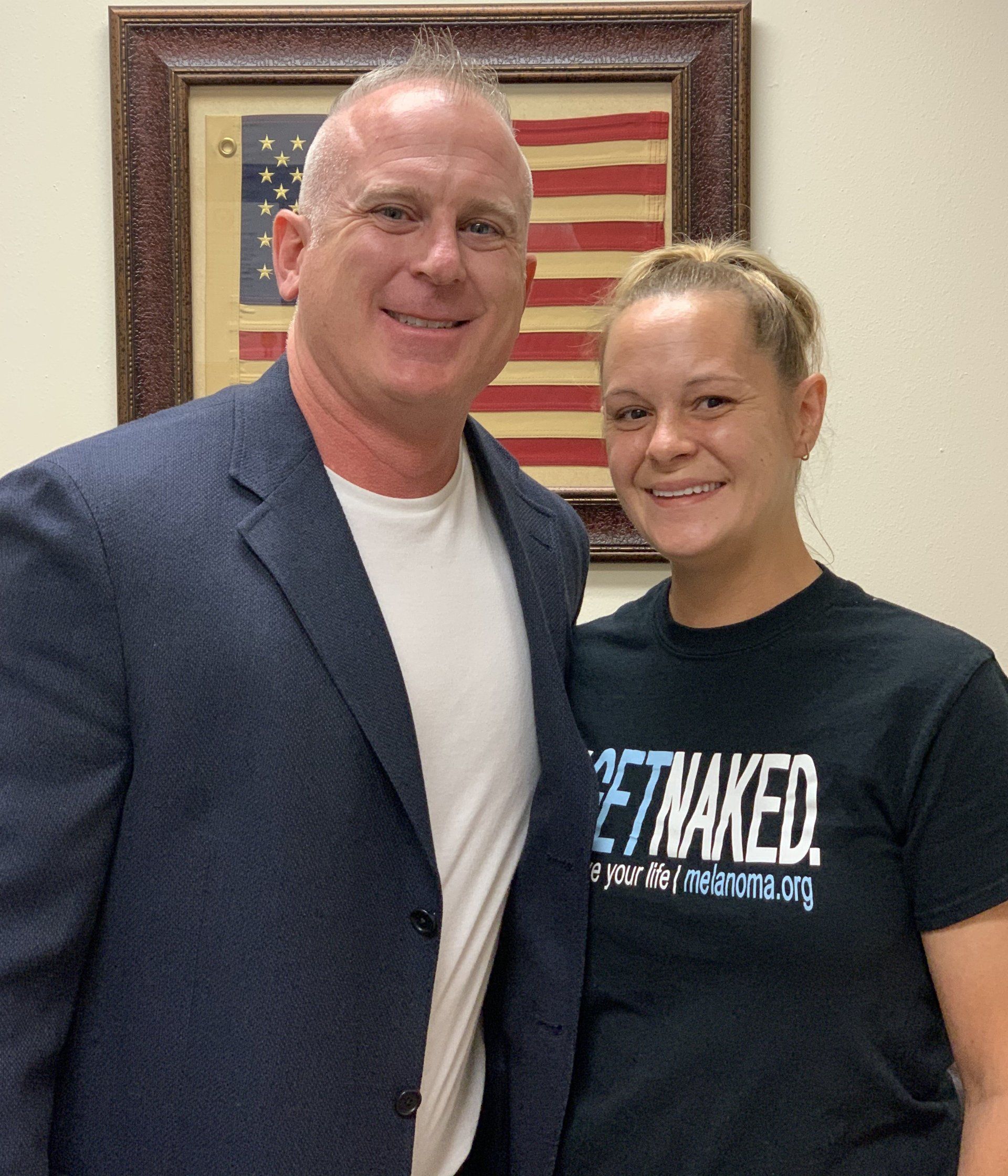 A man and a woman are posing for a picture in front of an american flag