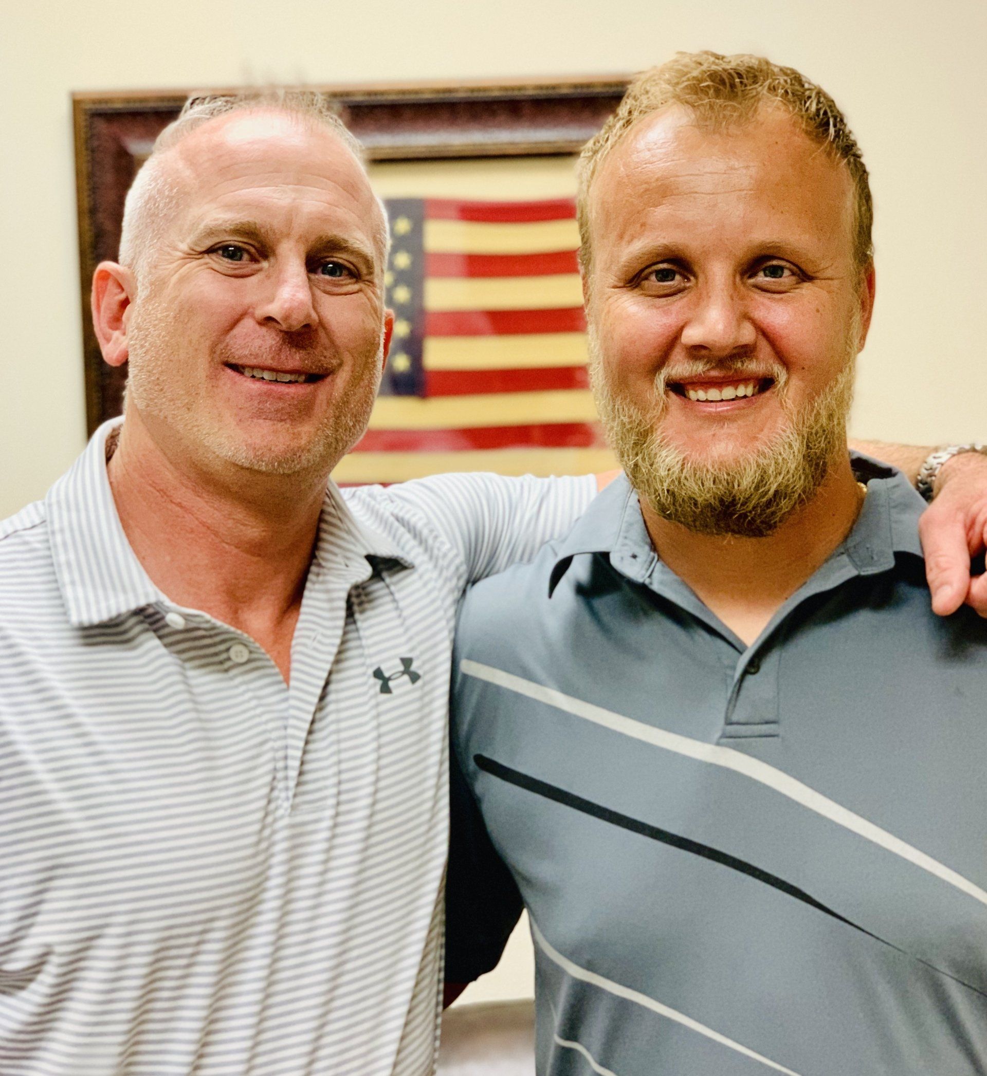 Two men are posing for a picture in front of an american flag.