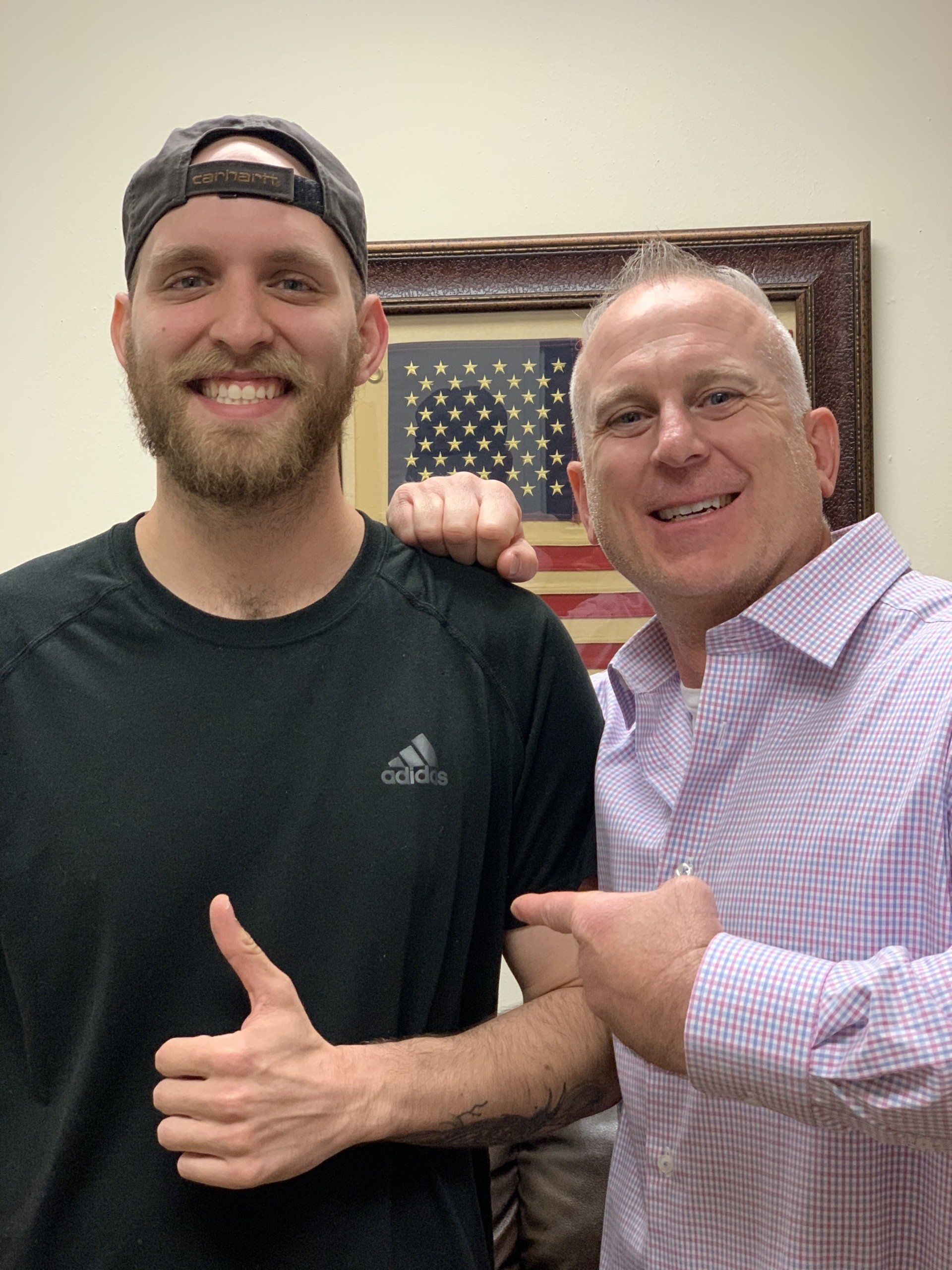 Two men are posing for a picture and one of them is giving a thumbs up.