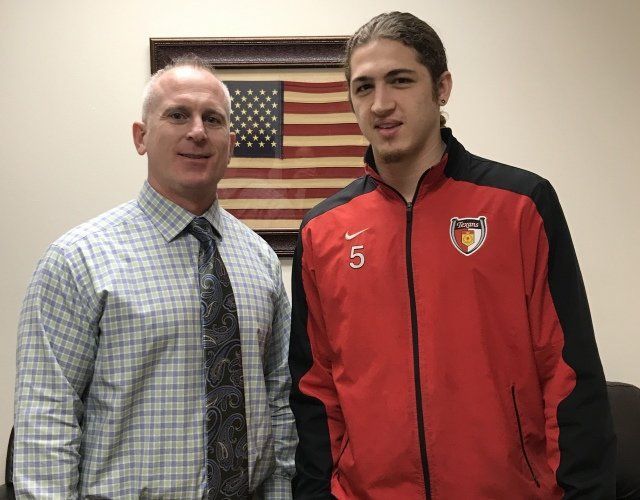 A man in a plaid shirt and tie stands next to a man in a red jacket with the number 5 on it