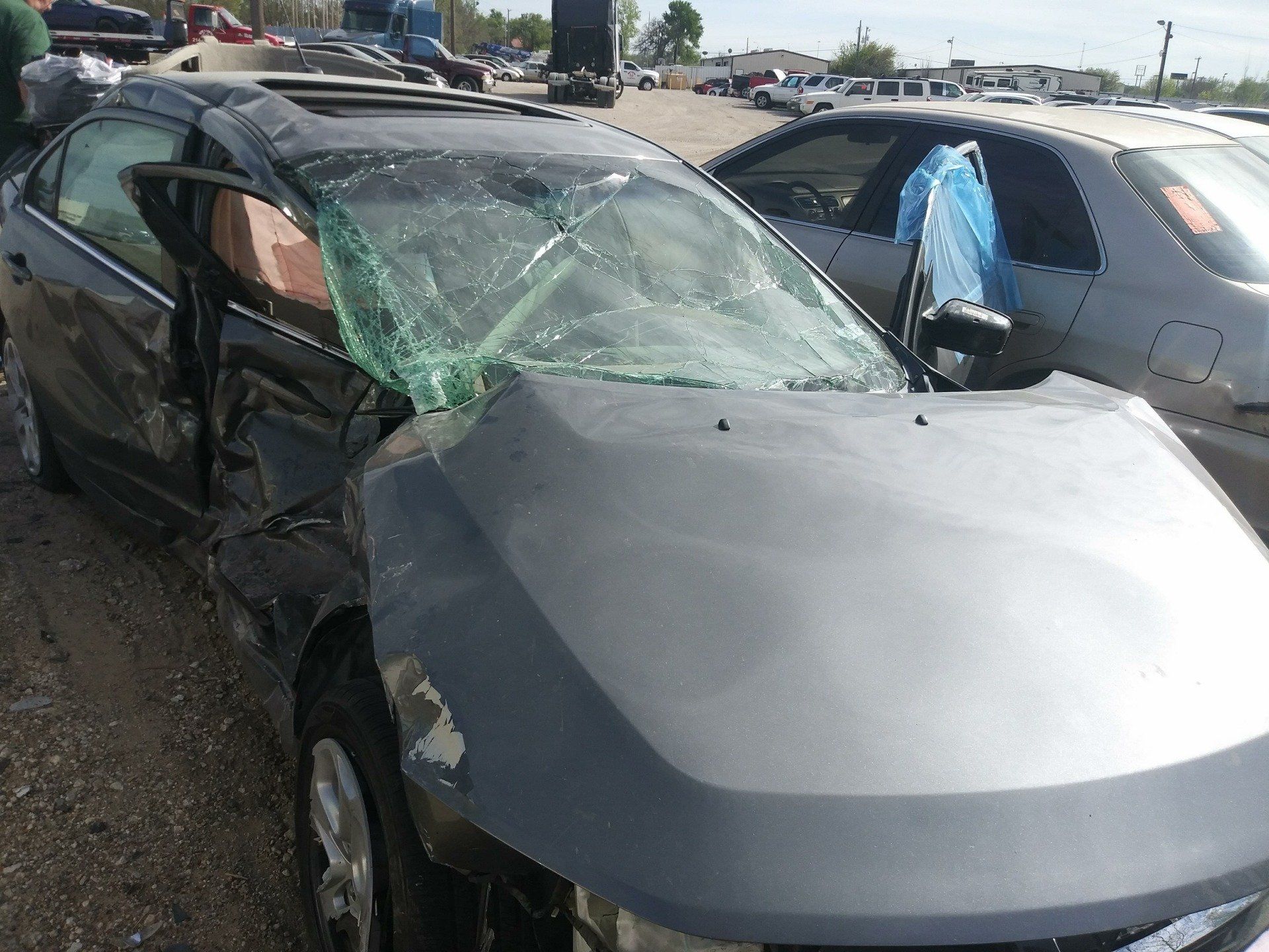 A gray car with a broken windshield is parked next to another car.