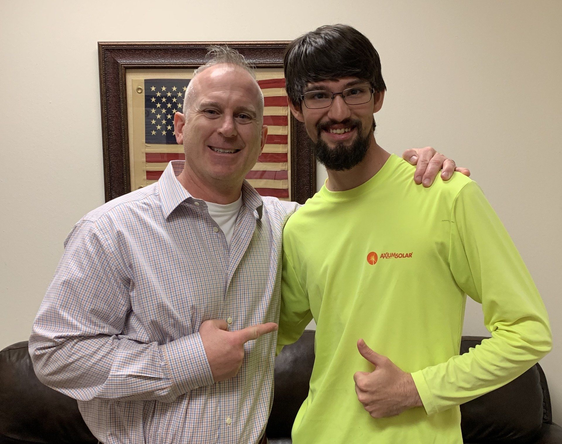Two men are posing for a picture in front of an american flag.