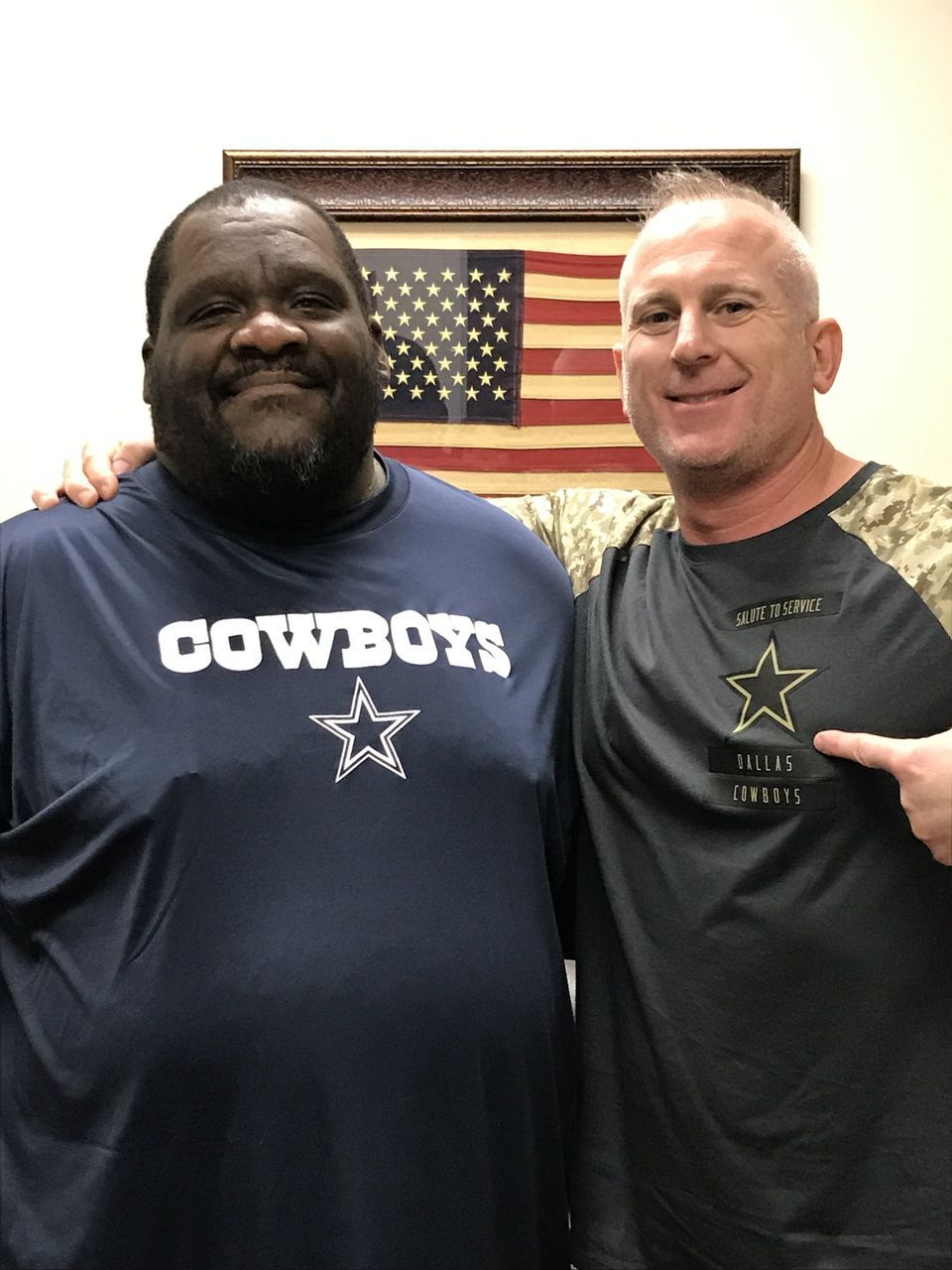 Two men are posing for a picture one is wearing a cowboys shirt