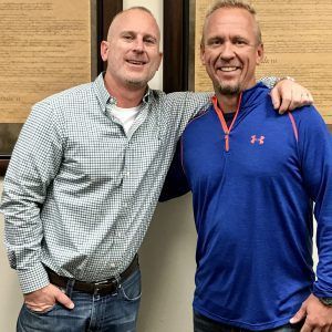 Two men are posing for a picture and one is wearing a blue under armour shirt.