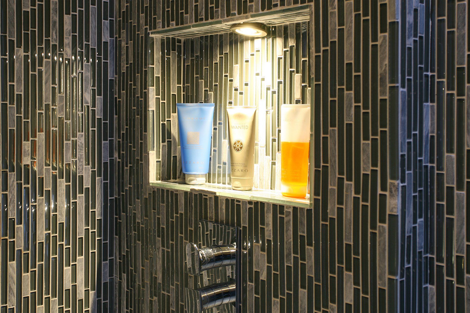 There is a shelf in the shower with bottles of lotion on it.