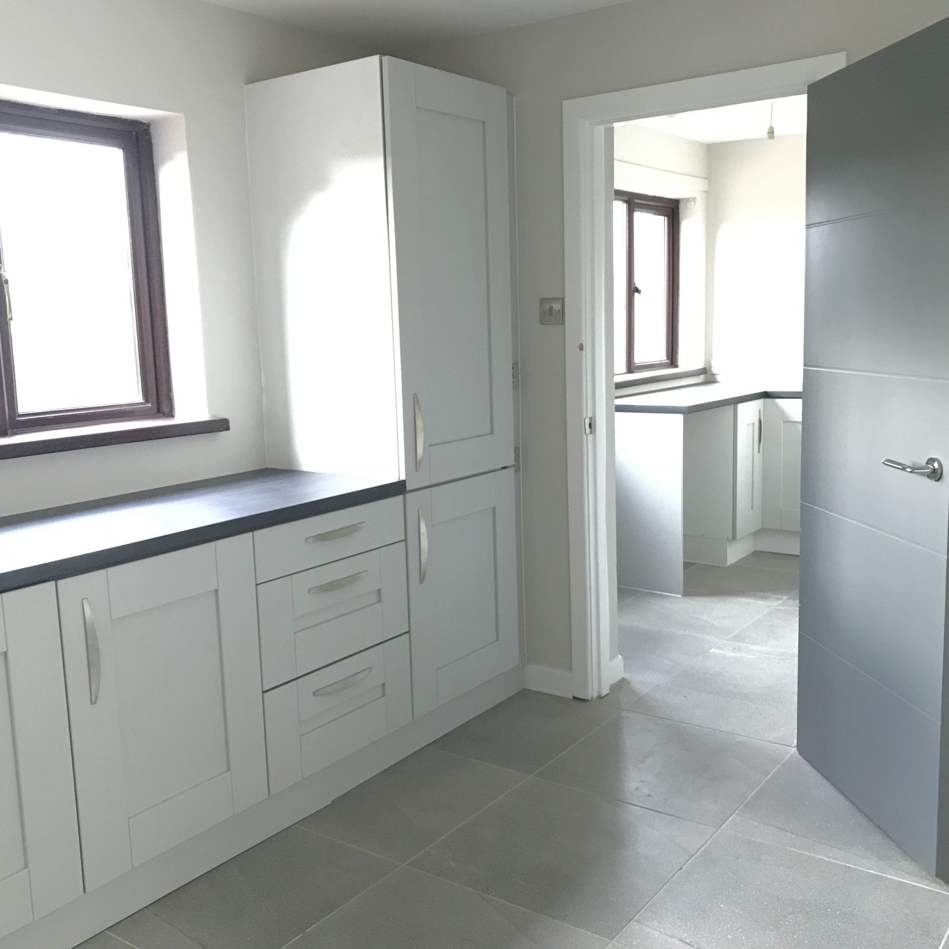 A kitchen with white cabinets and a gray door