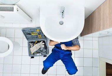 A plumber is fixing a sink in a bathroom.