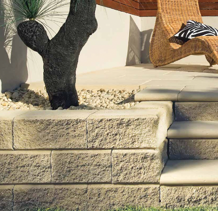 A wicker chair sits on a patio next to a stone wall