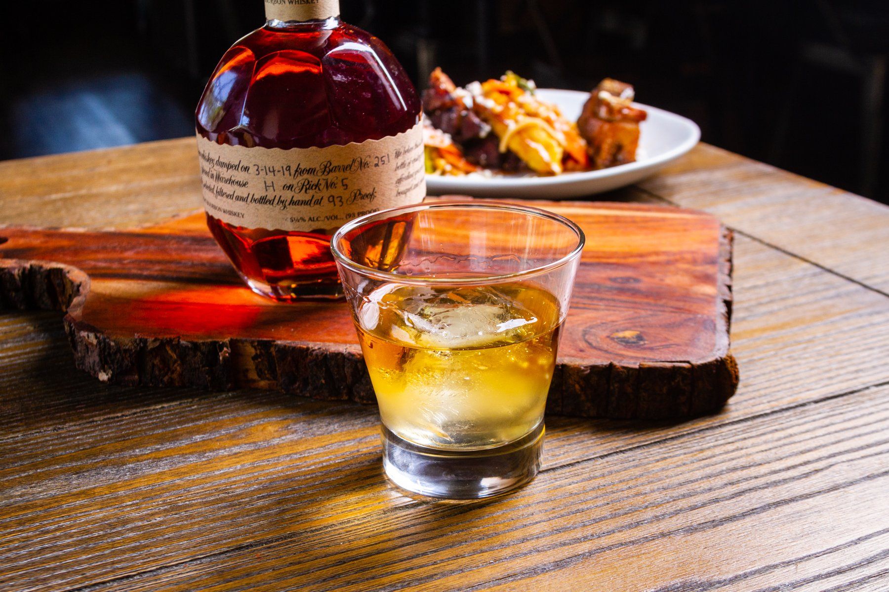 A bottle of whiskey and a glass of whiskey are on a wooden table.