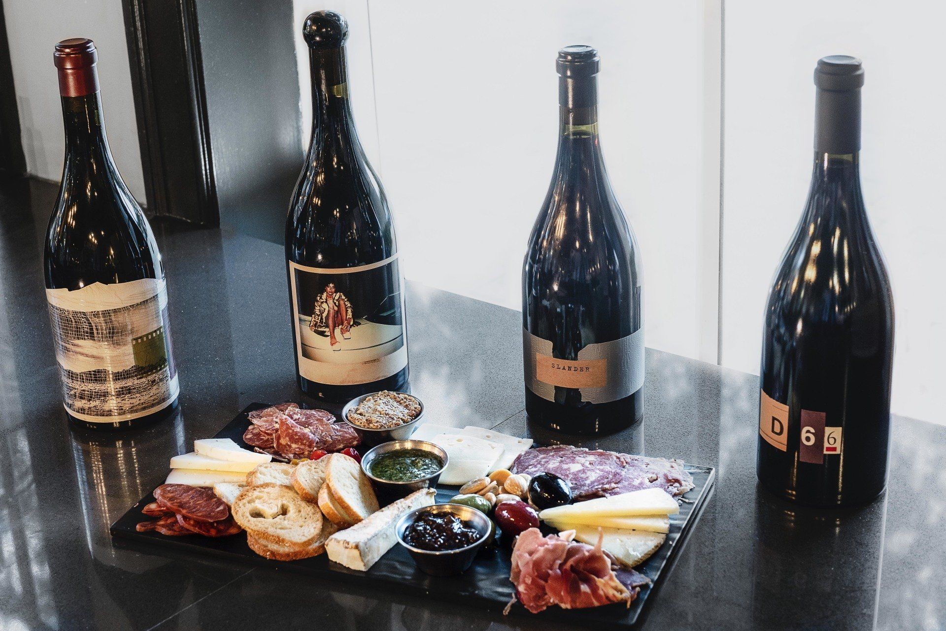 Four bottles of wine are sitting on a table next to a tray of food.
