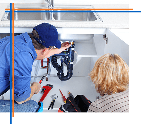 A plumber is fixing a sink in a kitchen while a woman looks on.