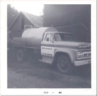 Old truck with tank parked next to a barn. It has