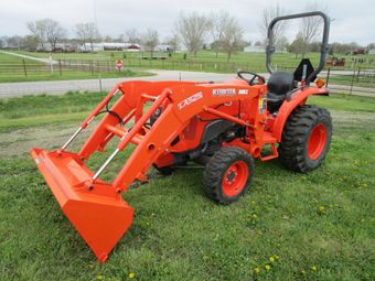 An orange tractor with a bucket attached to it is parked in a grassy field.