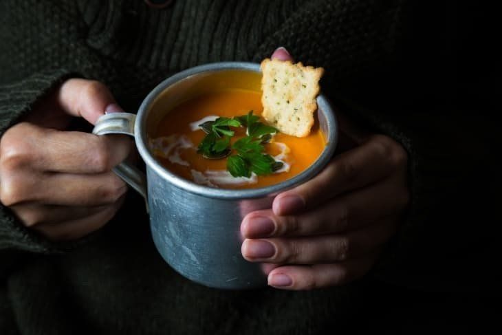 A person is holding a cup of soup with a cracker in it.