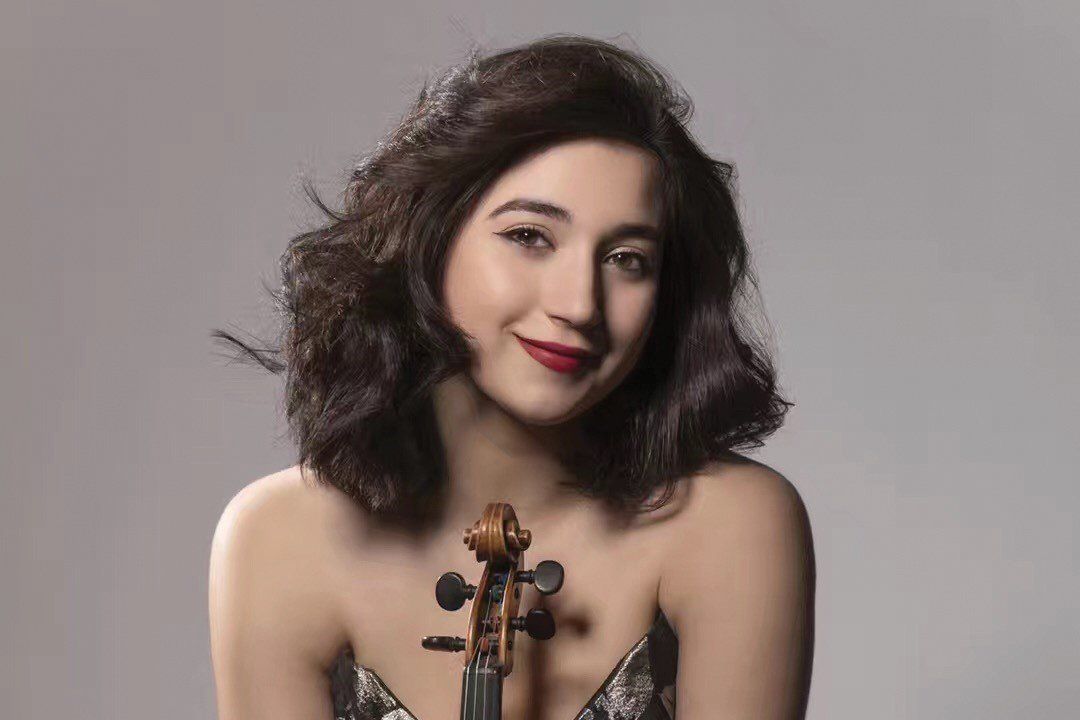 Une femme tient un violon à la main et sourit.