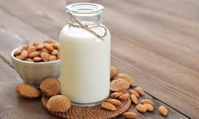 Une bouteille de lait d'amande à côté d'un bol d'amandes sur une table en bois.