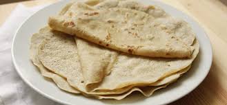 Une assiette blanche surmontée d'une pile de tortillas sur une table en bois.