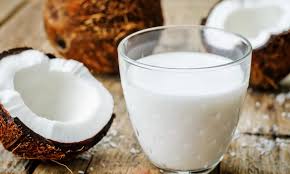 Un verre de lait de coco est posé sur une table en bois à côté des noix de coco.