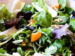 Un gros plan d'une salade avec de la laitue, des oranges et des pignons de pin.