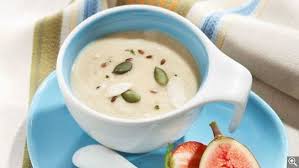 Un bol de soupe est sur une assiette bleue à côté d'une figue.
