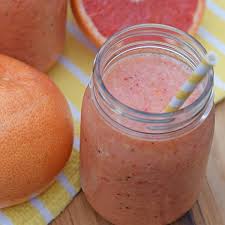 Un smoothie dans un pot avec une paille à côté de pamplemousse sur une table.