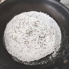 Une casserole remplie de poudre blanche et de graines noires.