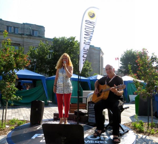 Un homme jouant de la guitare et une femme chantant devant une banderole qui dit