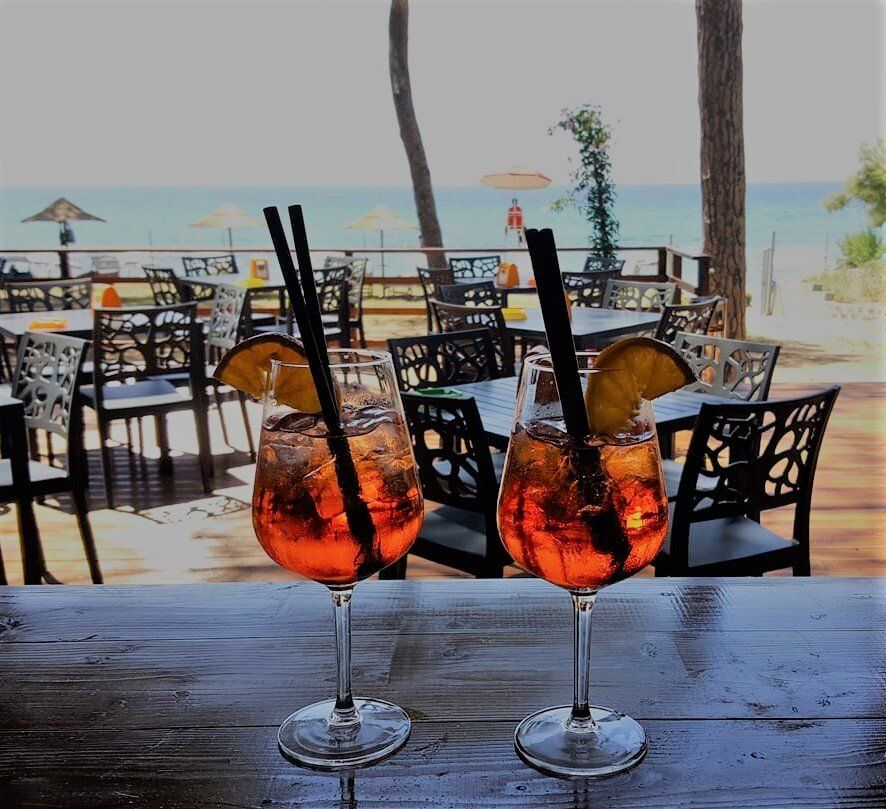 Due cocktail Aperol Spritz in un bar con una spiaggia e un ristorante sullo sfondo.