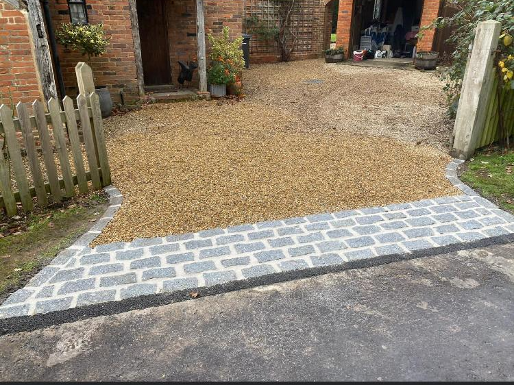 Driveway with gravel, bordered by brick pavers, leading to a brick building.