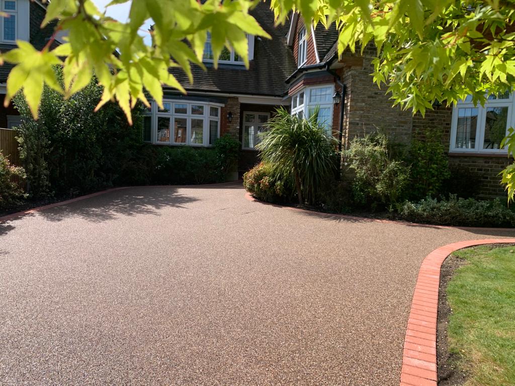 Resin-bound driveway in front of a brick house with a green lawn and plants.