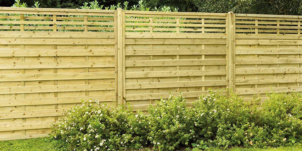 Wooden fence with horizontal slats and a lattice top, behind green bushes.