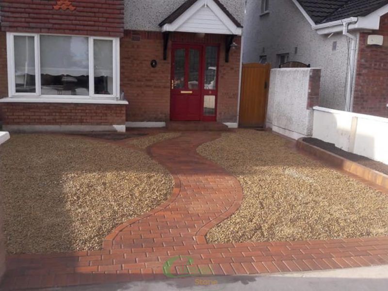 Red brick path leads to red door, surrounded by gravel driveway, brick home exterior.