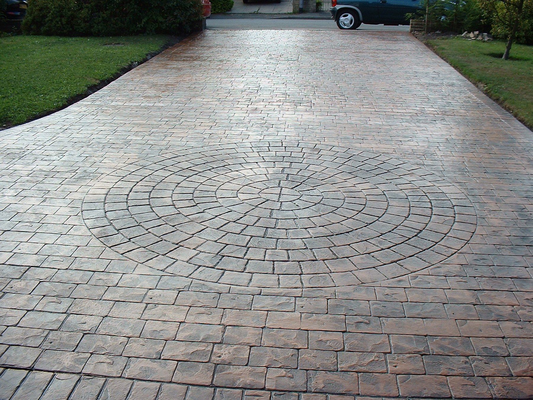 Driveway with textured concrete, featuring a circular brick pattern in the center and brick-like edging.