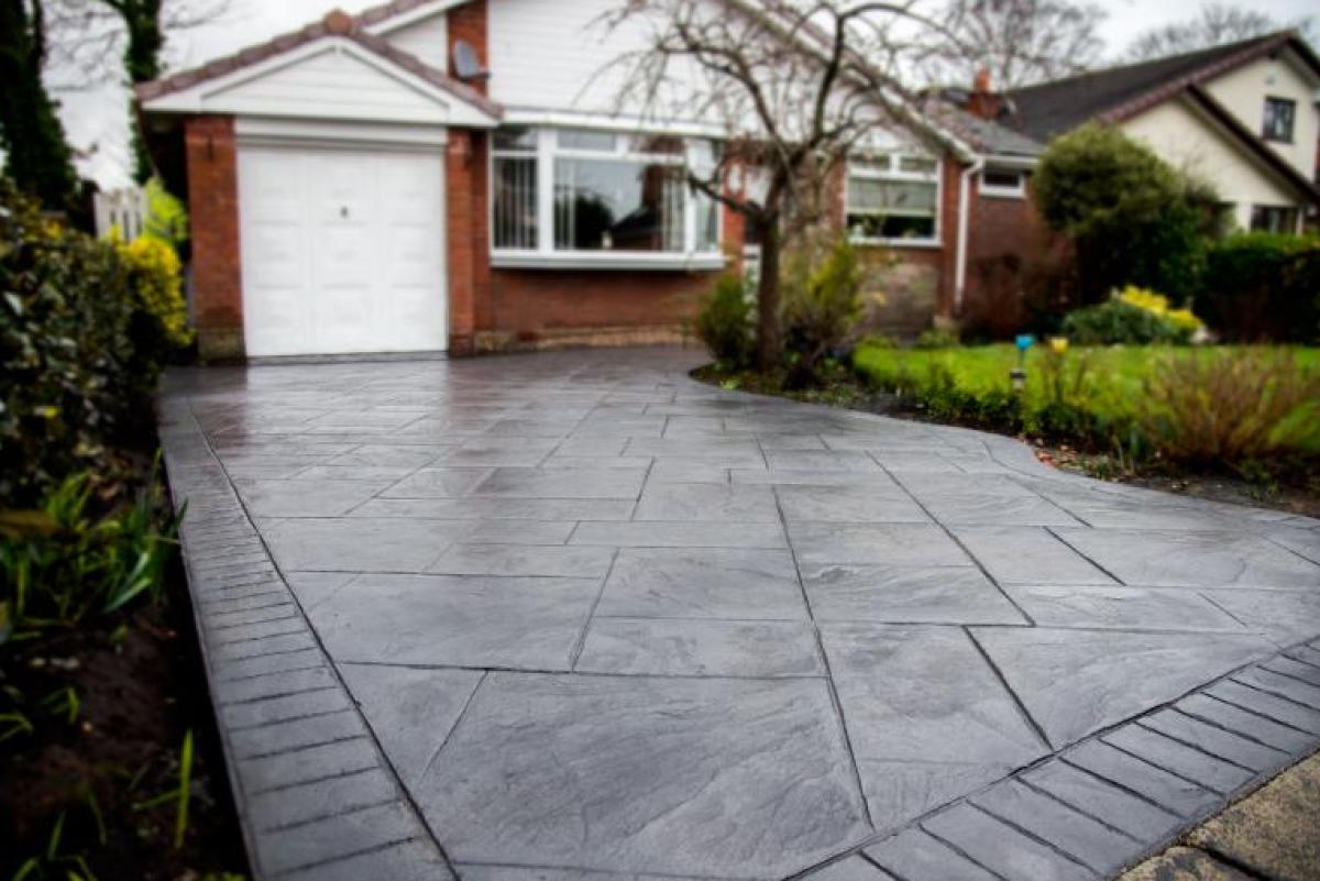 Gray patterned concrete driveway in front of a brick house with a garage door and small lawn.