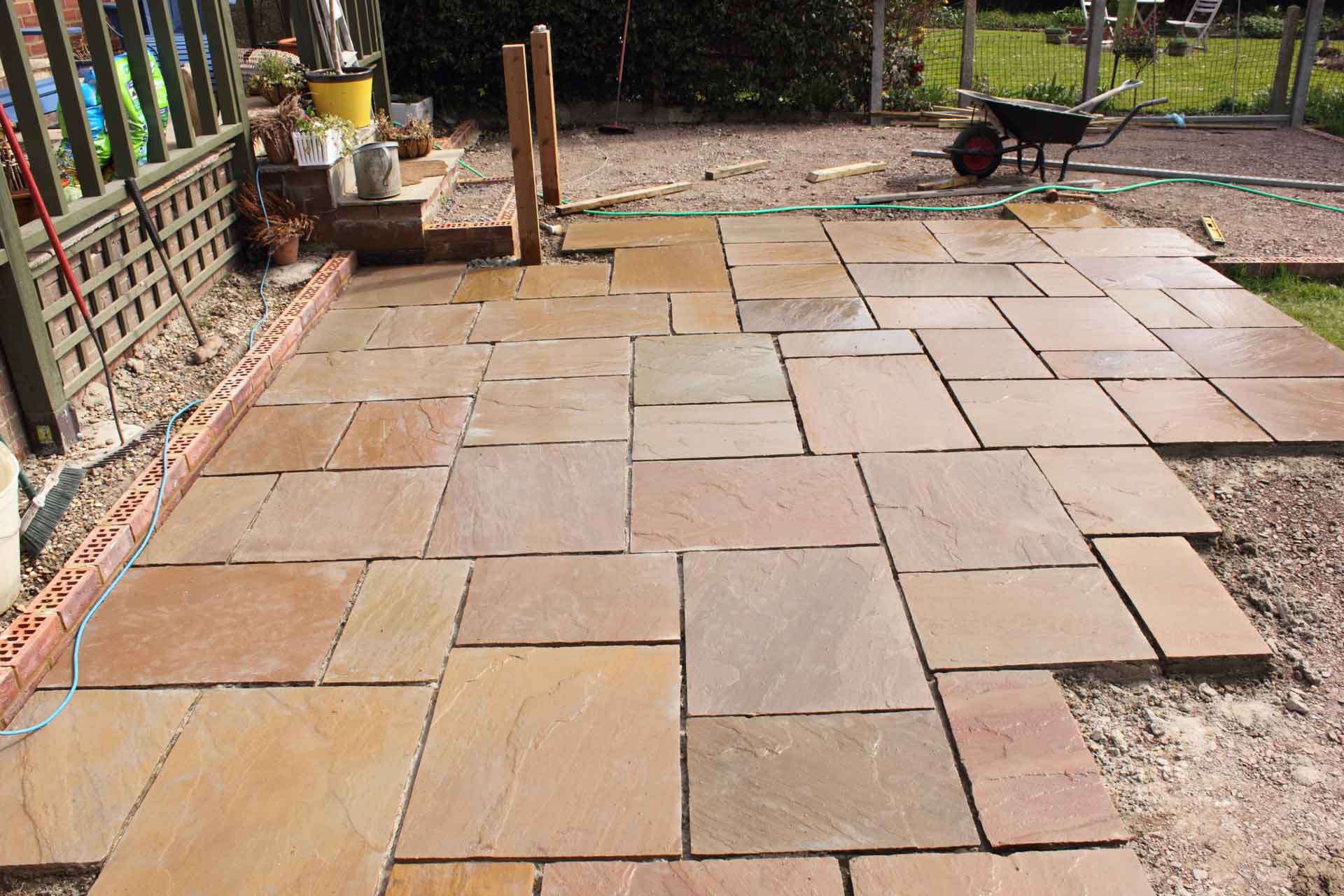 Patio construction: Brown sandstone paving stones laid in a backyard, with tools and garden visible.