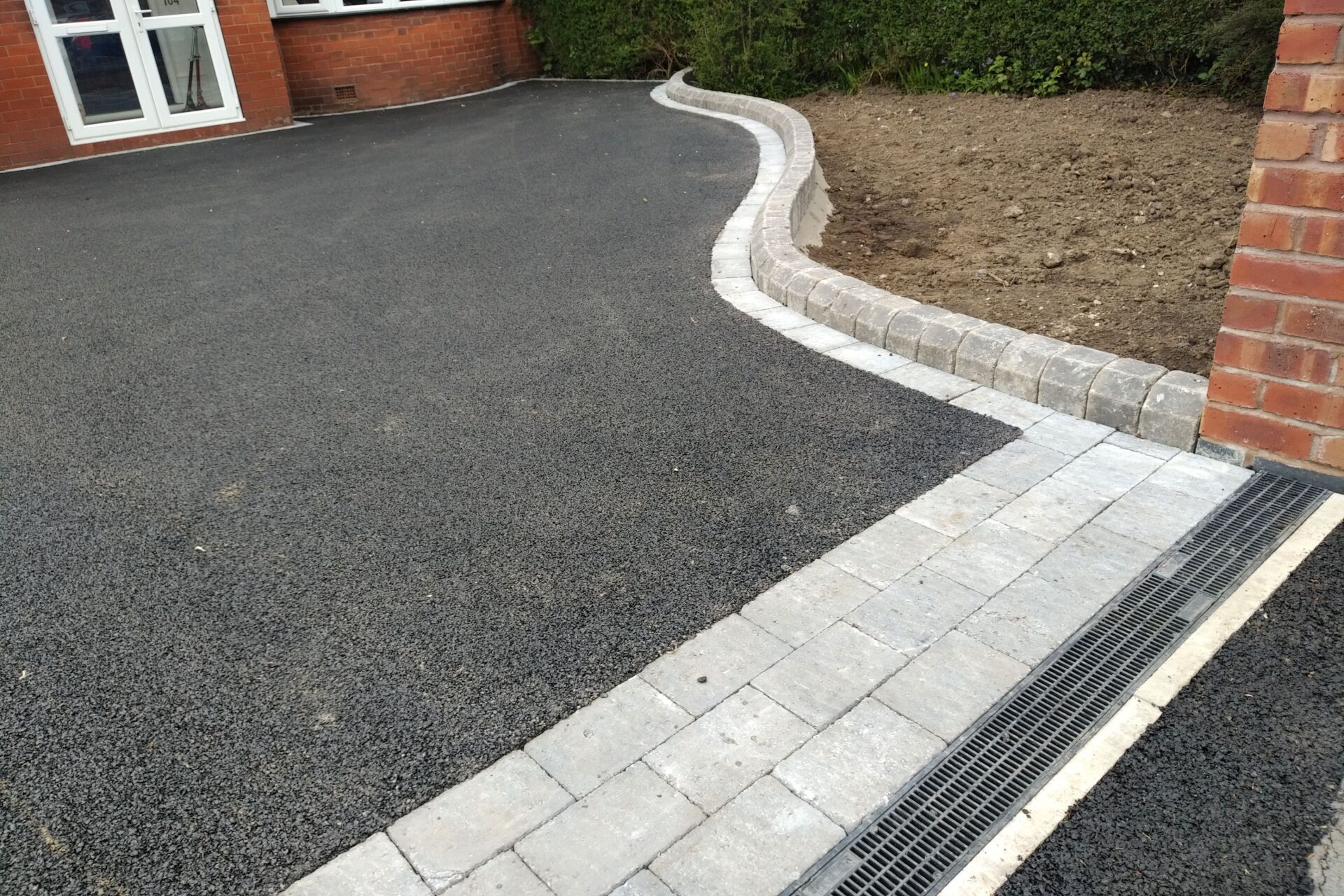 Black asphalt driveway with gray brick border and pathway.