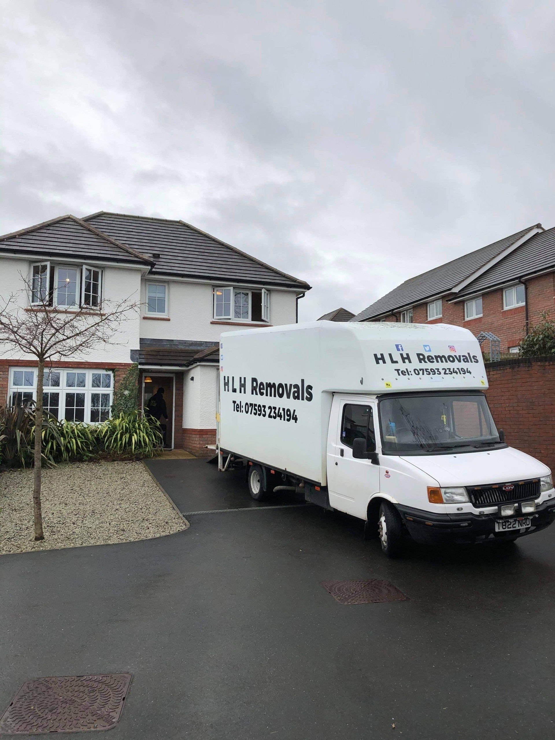 White moving truck parked outside a house on a wet street under overcast skies.