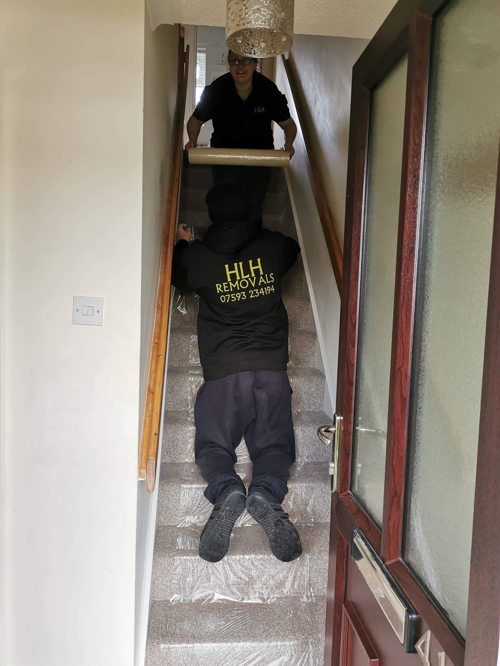 Person moving furniture up a narrow carpeted staircase with another person above.
