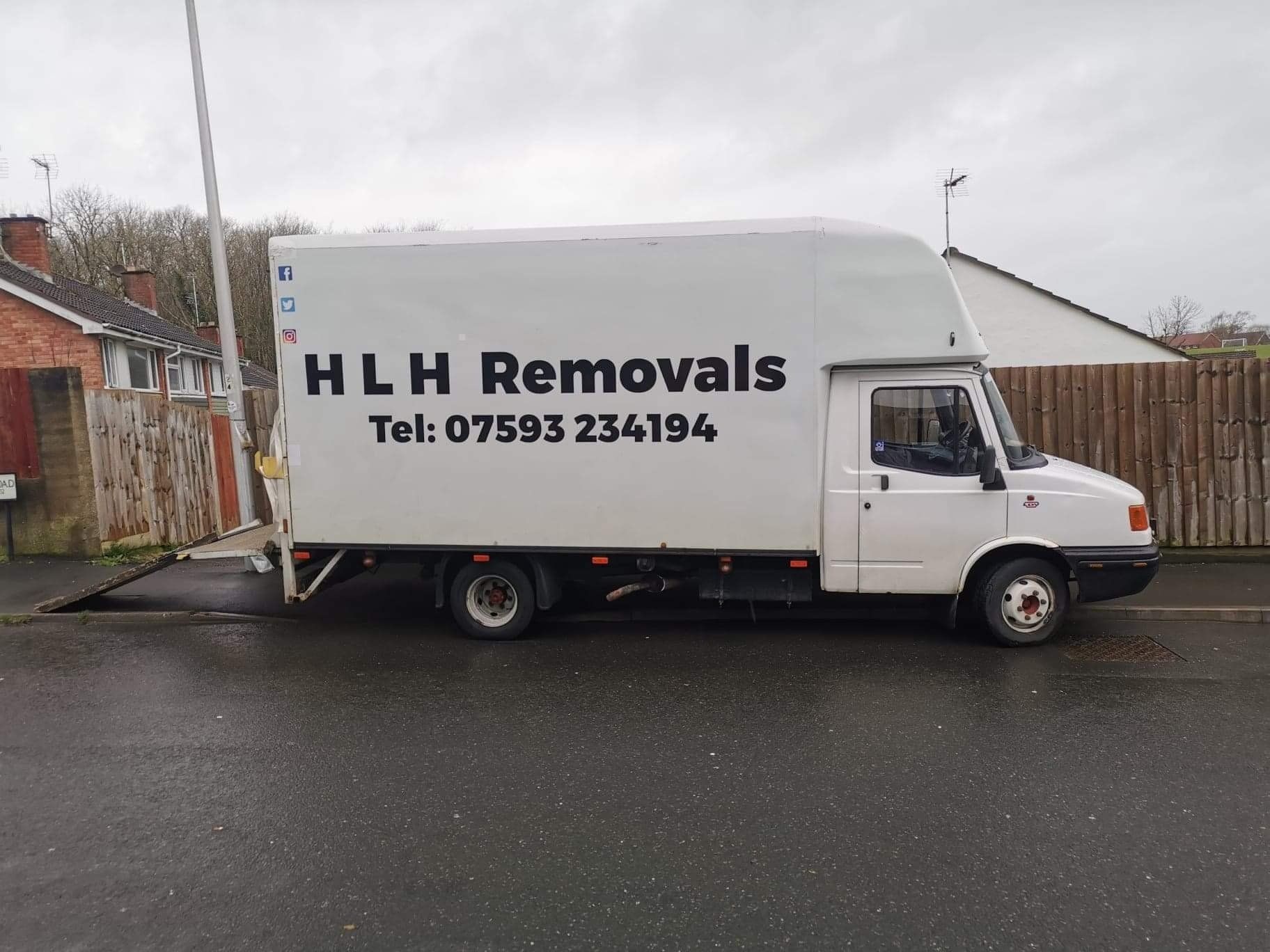 White HLH Removals van parked on a wet street, with company name and phone number on the side.