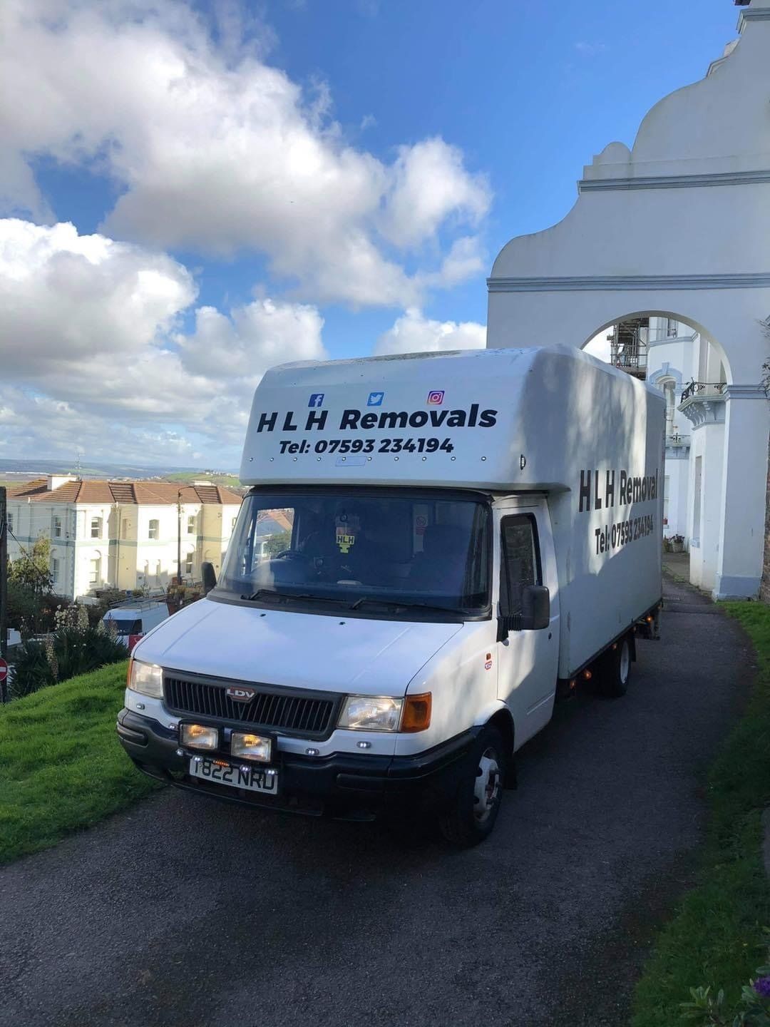 White H & F Removals van parked on a driveway beside a white building under a blue sky with clouds