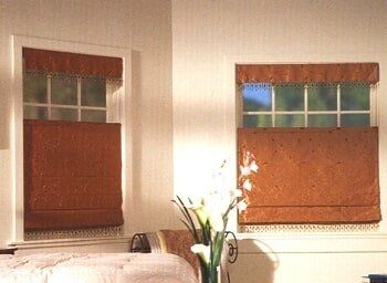 A bedroom with a bed and two windows with roman shades