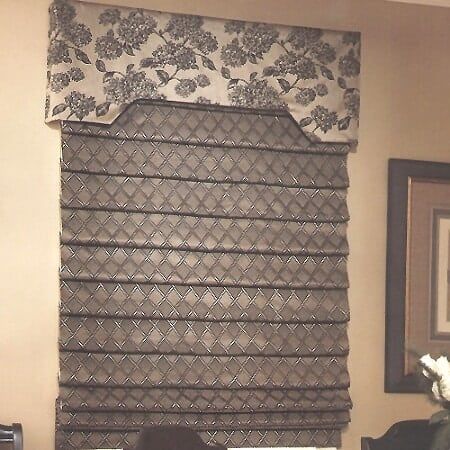 A window with a roman shade and a floral valance