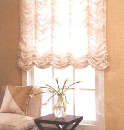 A vase of flowers sits on a small table in front of a window