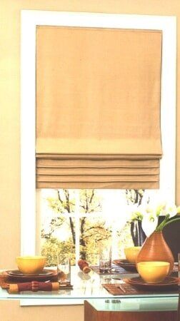 A window with a roman shade and a table with bowls on it