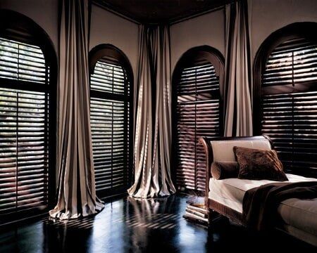A bedroom with arched windows and shutters on the windows