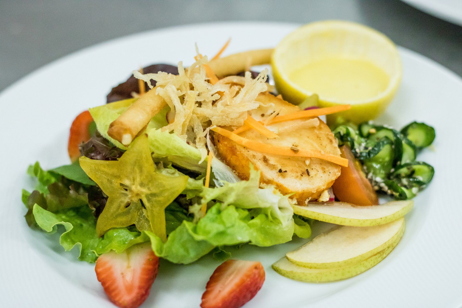 Uma salada com morangos, maçãs, cenouras e frango em um prato branco.