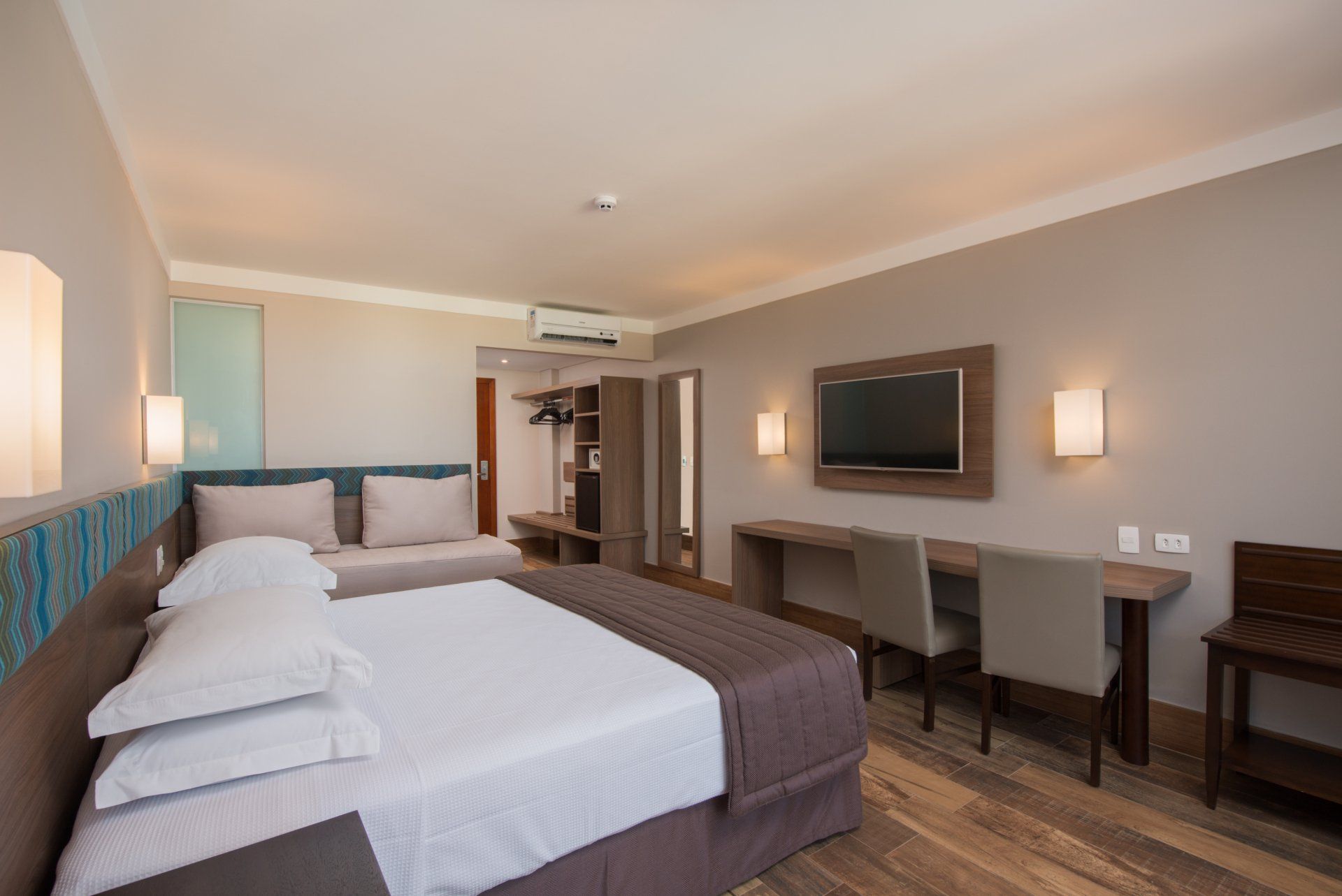 Um quarto de hotel com duas camas, uma escrivaninha, cadeiras e uma TV de tela plana.